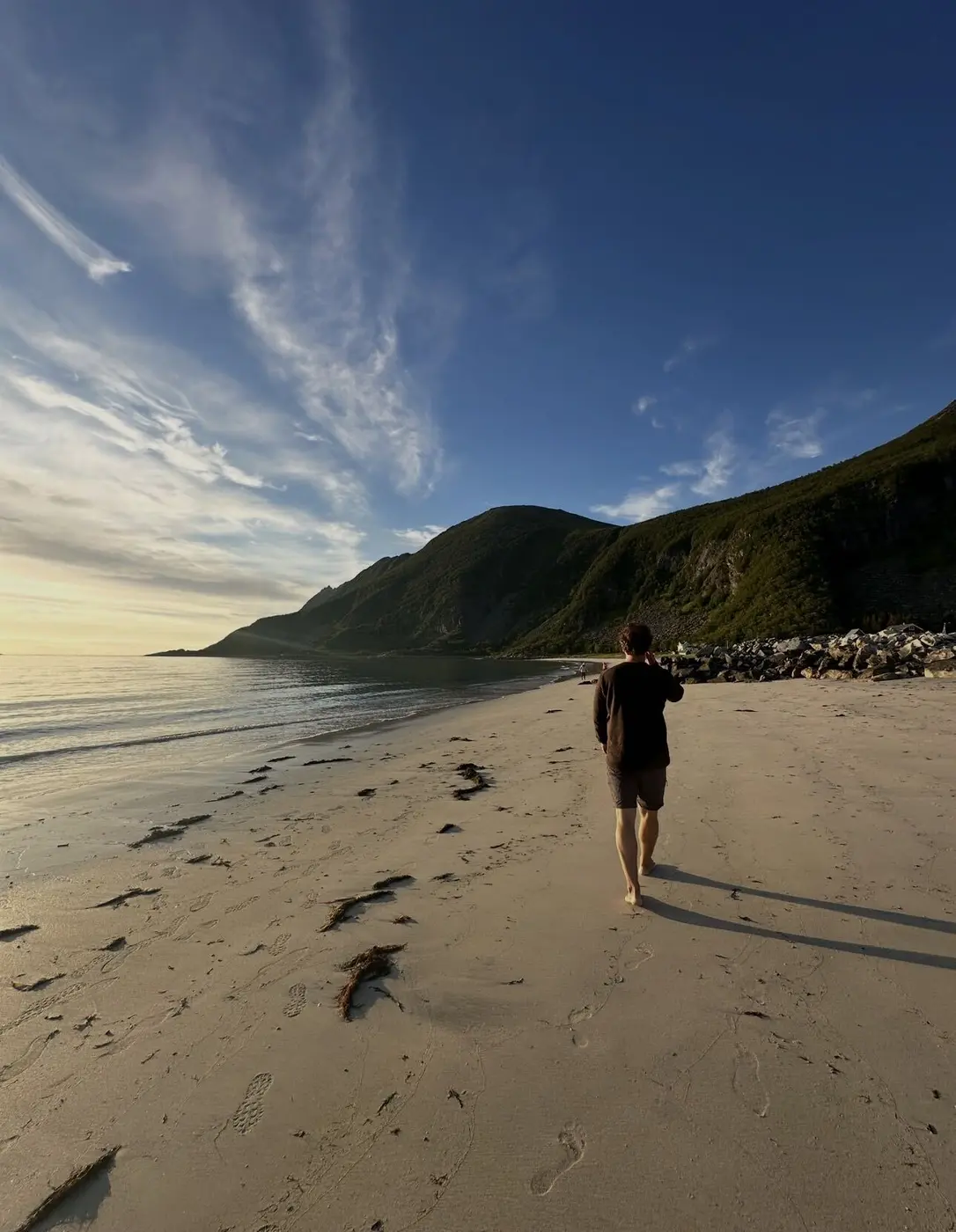 A traveller walking a quiet Norwegian beach at golden hour